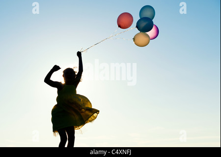 Silhouette of a young girl jumping with coloured balloons at sunset