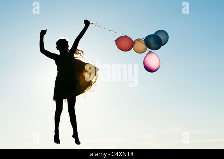Silhouette of a young girl jumping with coloured balloons at sunset