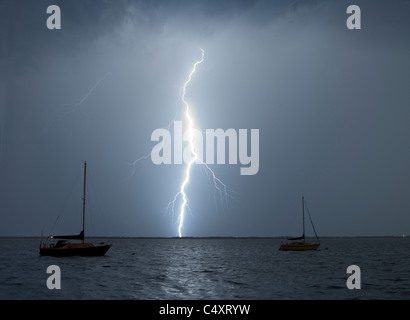 A lightning strike over water near a couple of sailboats. Stock Photo