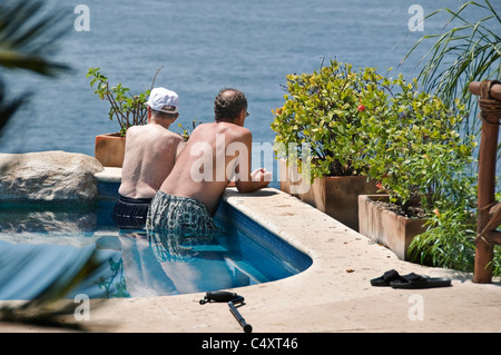 A senior adult male and his elderly father relax in a swimming pool overlooking the Pacific Ocean in San Pancho, Mexico. Stock Photo