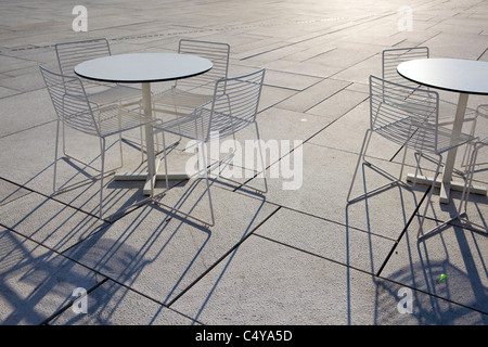 Rounded table/s and chairs on a tiled floor shadow is revealed through a descending sunset Stock Photo