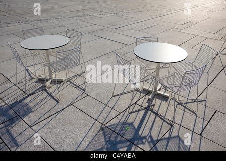 Rounded table/s and chairs on a tiled floor shadow is revealed through a descending sunset Stock Photo