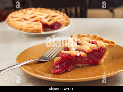 slice of cherry pie removed from a whole pie on a table Stock Photo