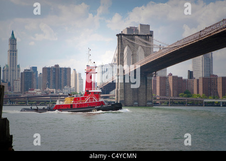 Sailing red boat cruises under Brooklyn Bridge on a cloudy day Stock Photo
