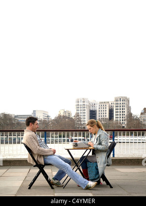 Man and woman sitting on chairs at a small table with a typewriter at the South Bank in London overlooking the Thames Stock Photo