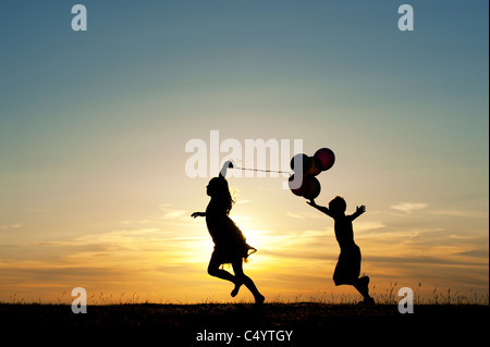 Silhouette of a young girl and boy running with balloons at sunset Stock Photo