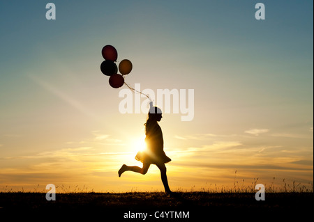 Silhouette of a young girl running with balloons at sunset Stock Photo