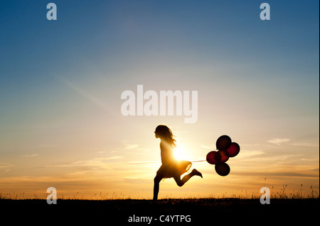 Silhouette of a young girl running with balloons at sunset Stock Photo