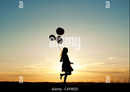 Silhouette of a young girl running with balloons at sunset Stock Photo