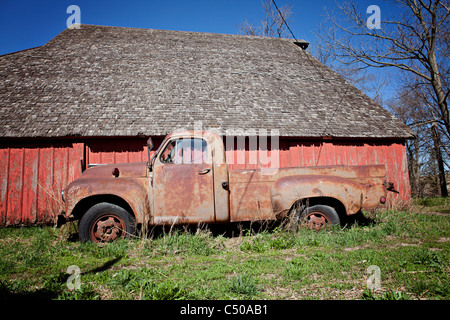 Old rusted truck sitting in front of old red barn in Iowa. Stock Photo