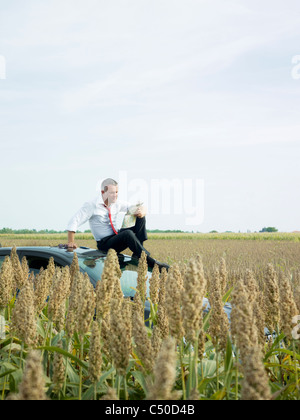 Caucasian businessman sitting on top of car in field Stock Photo
