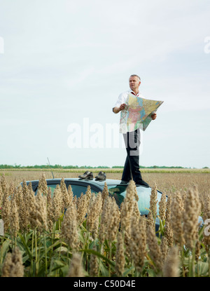 Caucasian businessman on top of car in field looking at map Stock Photo