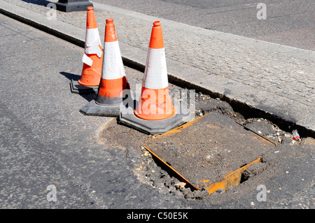 Potholes around manhole cover in London street marked by road traffic cones England UK Stock Photo