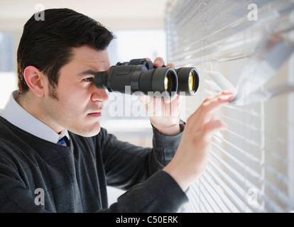 Hispanic businessman peering through window with binoculars Stock Photo