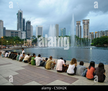 People sitting on a staircase in KLCC Park at the Petronas Twin Towers in front of the skyline with office buildings and hotels Stock Photo