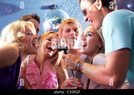 Portrait of joyous guys and girls singing at party in one microphone Stock Photo