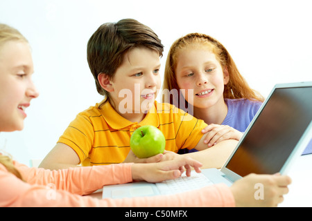 Portrait of smart schoolgirls and schoolboy looking at the laptop screen Stock Photo