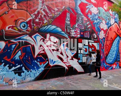 Paris, France, Two Teenage Girls Walking by Graffiti Artists Painting Wall, street art, People, city colour, urban art paris Stock Photo