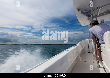 Thrill Seeking Adult male driving speedboat fast Florida Keys offshore Atlantic Ocean motion blur water spray blue sky stratus and cumulus clouds Stock Photo