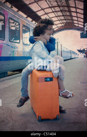 Brother and sister sitting together on suitcase waiting in train station Stock Photo