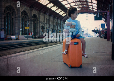 Little girl sitting on suitcase waiting in train station Stock Photo