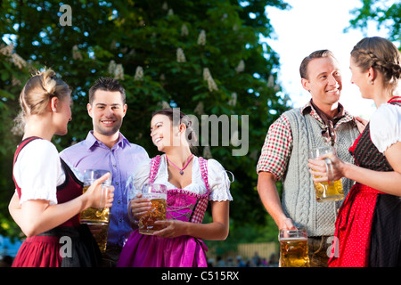 In Beer garden - friends in Tracht, Dindl and Lederhosen drinking a fresh beer and talk in Bavaria, Germany Stock Photo