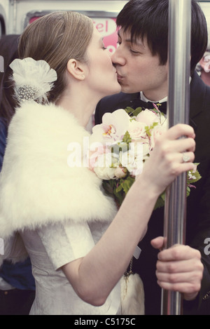 Bride and groom kissing on subway train Stock Photo