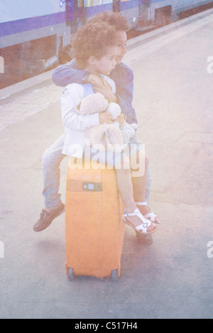 Brother and sister sitting together on suitcase waiting in train station Stock Photo