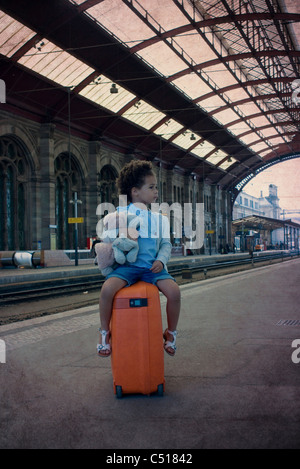 Little girl sitting on suitcase waiting in train station Stock Photo