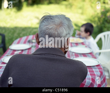 Senior man sitting at table outdoors, contemplating grandchild Stock Photo