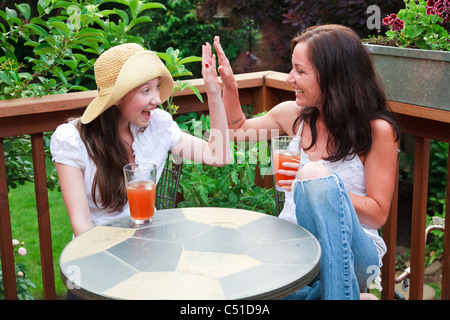 Mom and daughter sitting outside drinking tea laughing and giving each other a high five. Stock Photo