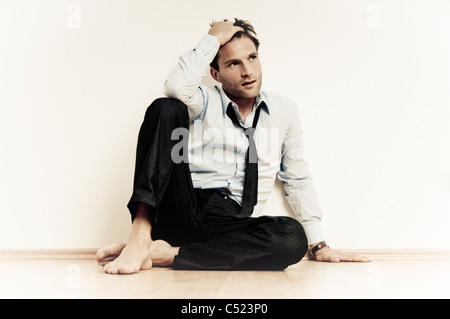 Man sitting casually on the floor, burn-out, stress, fatigue, isolation, loneliness and self-doubt Stock Photo
