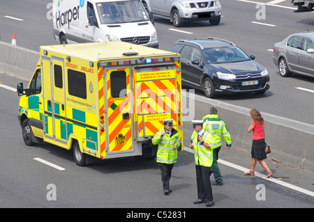 Paramedic with walking woman car crash accident victim at NHS emergency ambulance M25 motorway incident under bridge police at scene Essex England UK