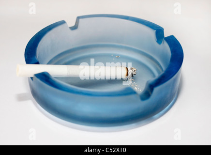 A lit cigarette burning in a blue glass ashtray Stock Photo