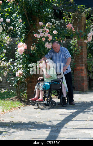 man pushing lady in wheelchair in rose gardens southsea hampshire england uk Stock Photo