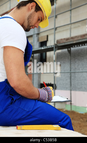 Manual worker on construction site writing on clipboard. Stock Photo