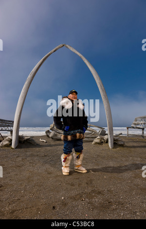 Male Inupiaq Eskimo hunter wearing his Eskimo parka , standing in front of a Bowhead whale bone arch and Umiaqs, Barrow, Alaska Stock Photo