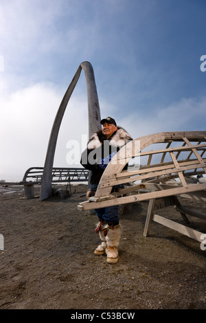 Male Inupiaq Eskimo hunter wearing his Eskimo parka , standing in front of a Bowhead whale bone arch and Umiaqs, Barrow, Alaska Stock Photo