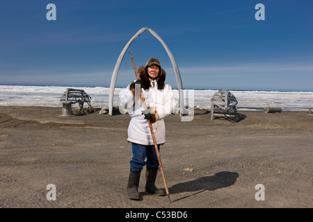 Male Inupiaq Eskimo hunter wearing his Eskimo parka , standing in front of a Bowhead whale bone arch and Umiaqs, Barrow, Alaska Stock Photo