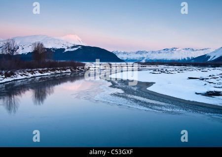 Morning alpenglow on the Kenai Mountains along the Turnagain Arm reflects in the outfall of Portage Creek, Alaska, Winter Stock Photo