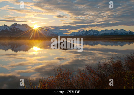 Sun rises over the Chugach Mountains with a pond and beaver lodge in the foreground, Chugach National Forest, Alaska Stock Photo