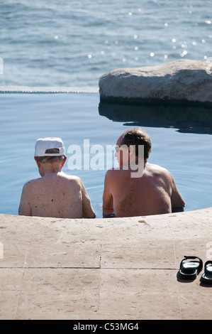 A senior adult male and his elderly father relax in a swimming pool overlooking the Pacific Ocean in San Pancho, Mexico. Stock Photo