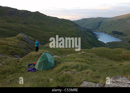 Hill Walker with Tent Enjoying the View Over Haweswater Reservoir from a Wild Camp Near Small Water Lake District Cumbria UK Stock Photo