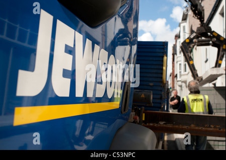 A workman wearing a hi-vis vest  watching a Jewson company truck lorry unloading and delivering heavy building supplies, UK Stock Photo