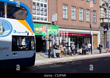 bus approaching queueing passengers at bus stop Stock Photo