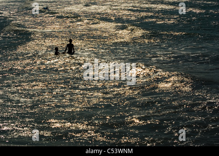 Adult and child playing in the sea as the sun goes down. Stock Photo