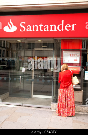 A woman getting cash from an ATM, Santander Bank, the Strand, London UK Stock Photo