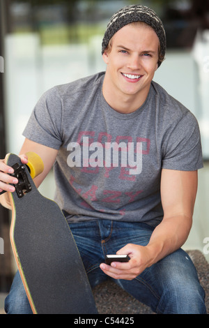 Portrait of a man holding skateboard and using mobile phone Stock Photo