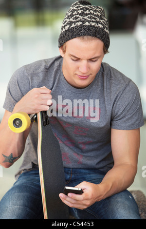 Young man holding skateboard and using a mobile phone Stock Photo