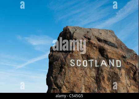 Scotland border stone at the Northumberland border in front of a white cross plane trail in the blue sky Stock Photo